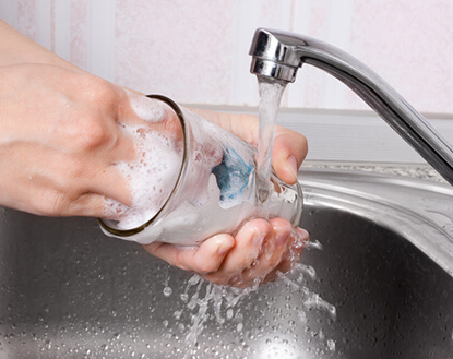 A hand washing a glass in a metal sink