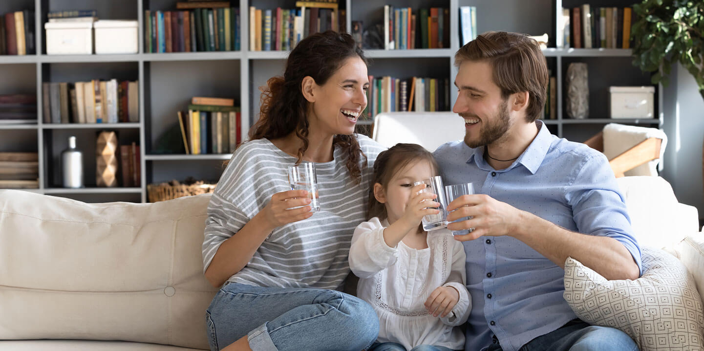 A man, woman, and young girl, sitting on a couch holding clear glasses