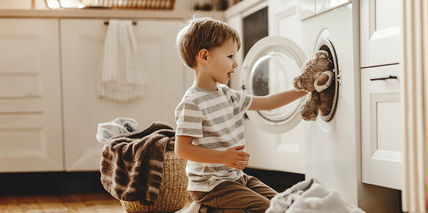 A young boy putting a stuffed teddy bear in the washing machine