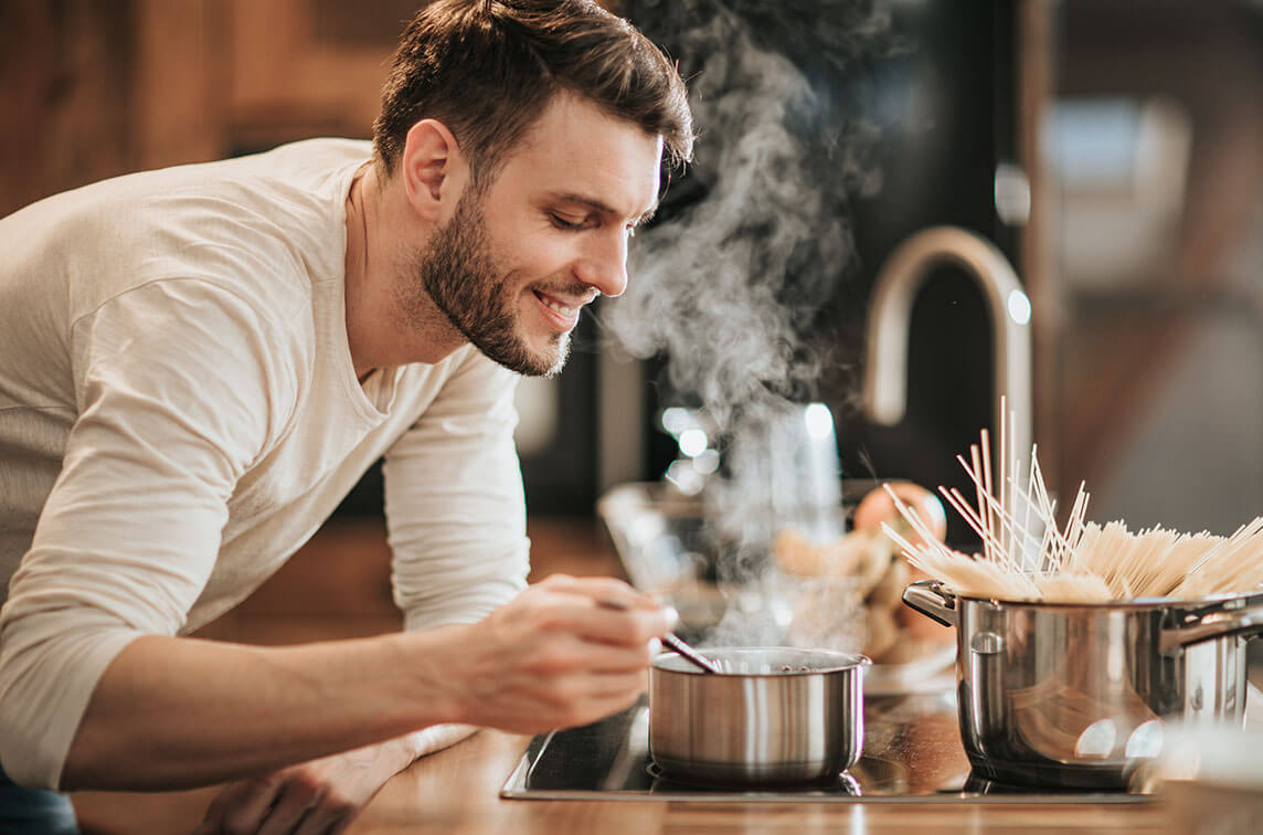 A man smiling as he is stirring a stainless steel pot