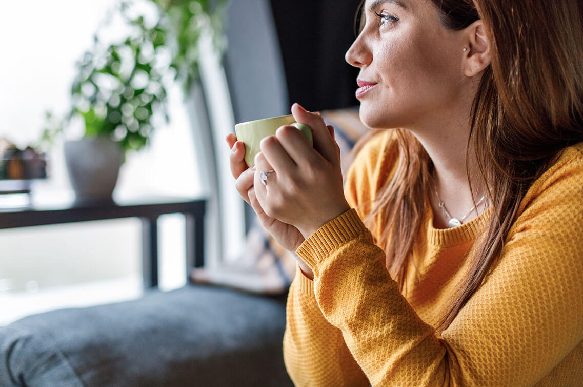 A woman holding a mug, looking out the window