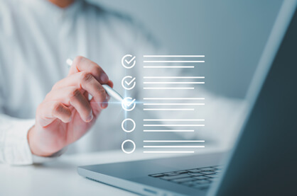 A person sitting in front of a laptop with a pen in hand, checking of a digital checklist